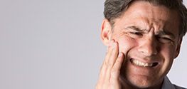 Man grimacing and holding cheek in pain